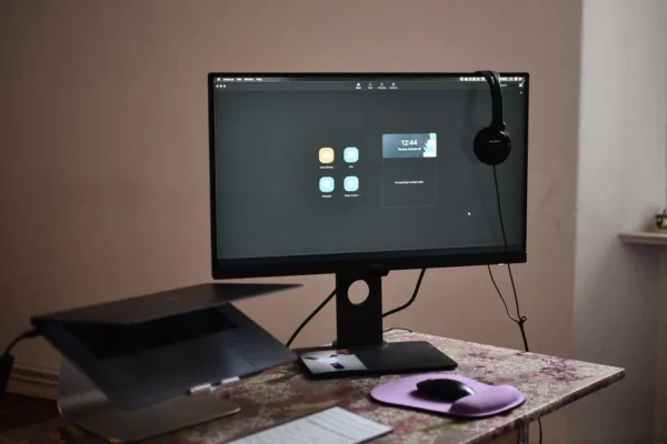 Contemporary computer with headphones hanging on monitor placed on table with laptop keyboard and mouse at convenient workplace in room