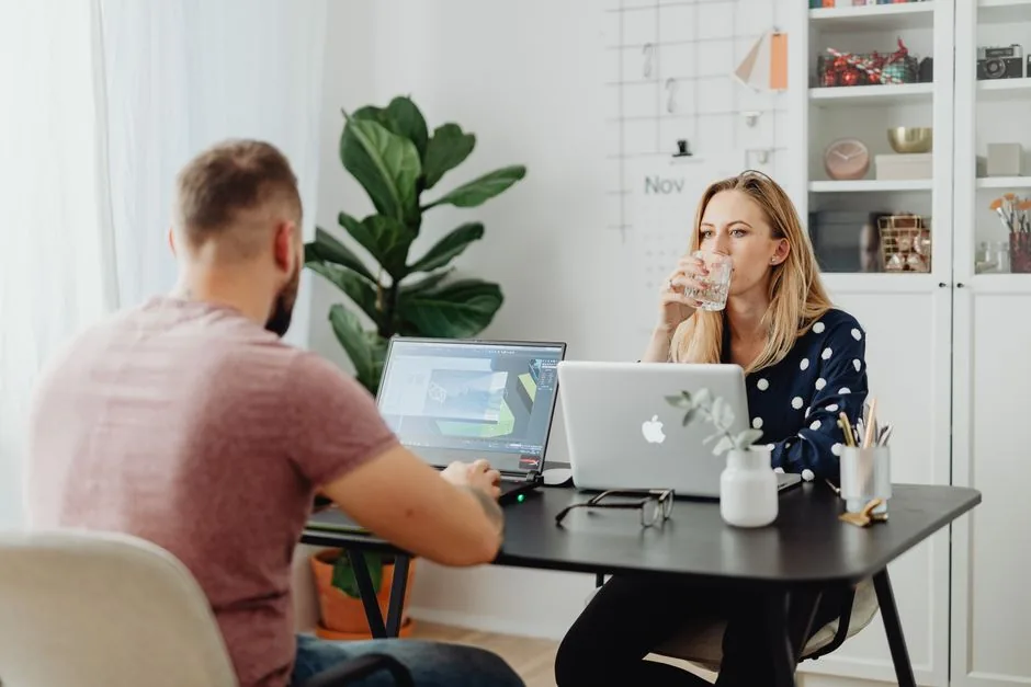 Two colleagues working in a stylish office space with laptops and beverages.